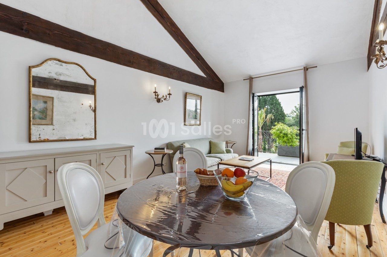 Salle de séjour lumineuse avec table à manger, canapé, miroir mural, et vue sur un jardin depuis une porte vitrée.
