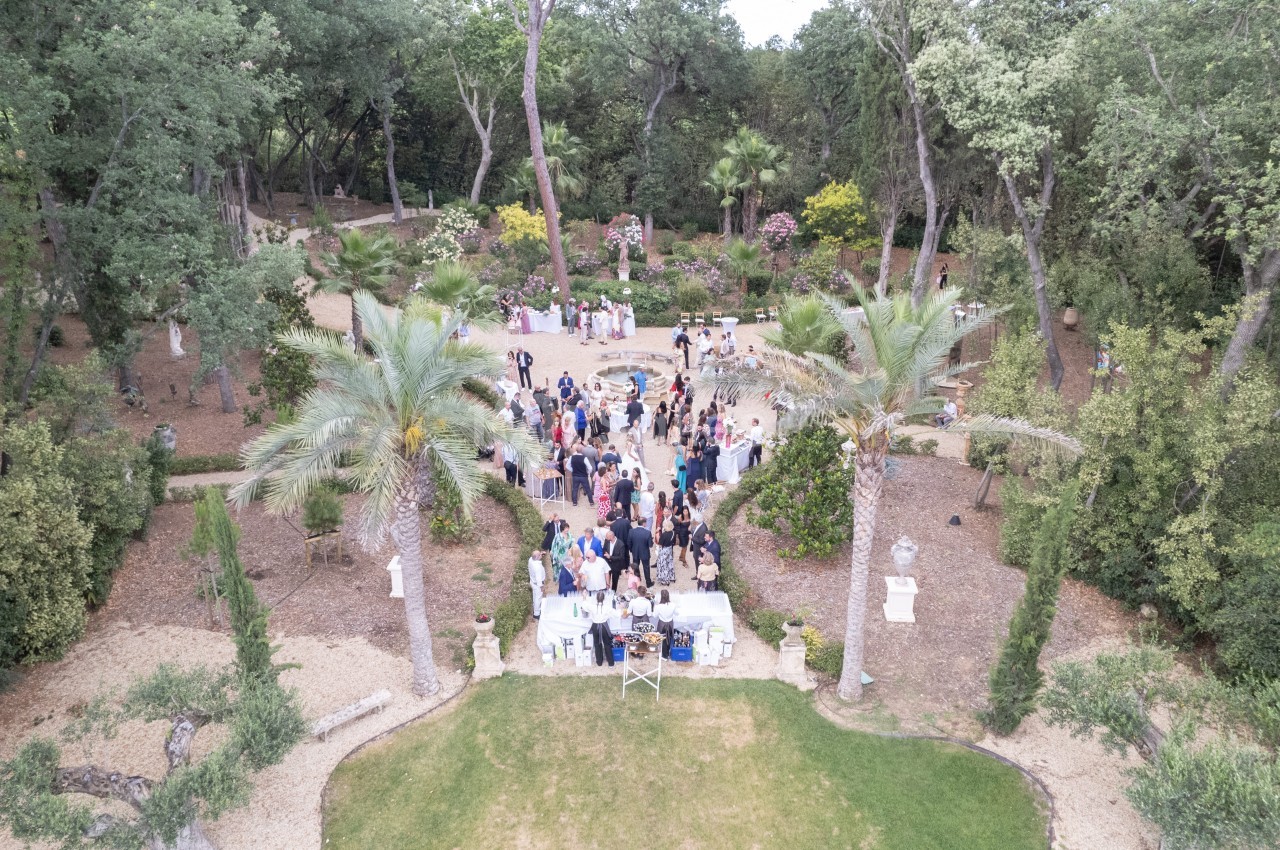 Vue aérienne d'un rassemblement en plein air dans un jardin arboré avec des tables et des invités.