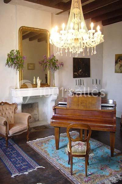 Salle avec un piano en bois, un lustre, un miroir doré, des tapis colorés et des meubles anciens.