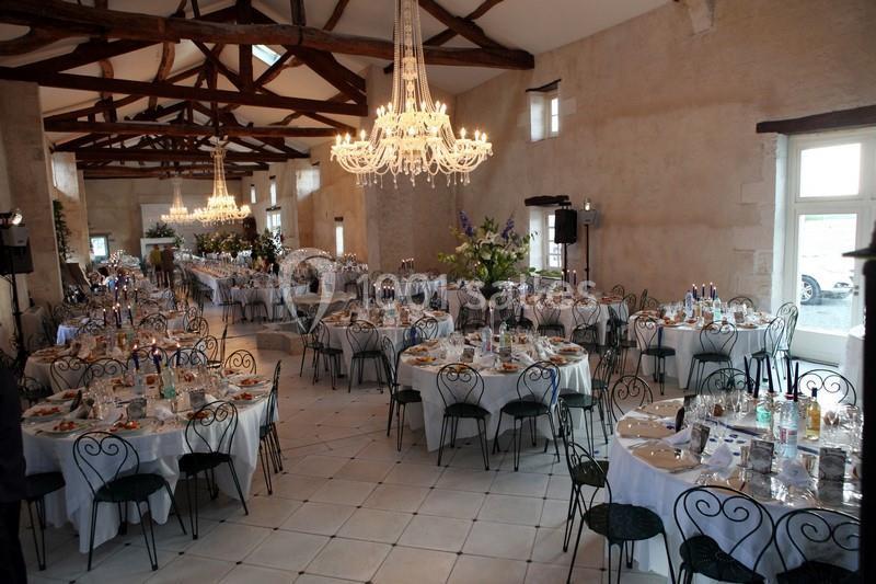 Salle de réception décorée avec des tables rondes dressées, des chaises en fer forgé et des lustres suspendus.