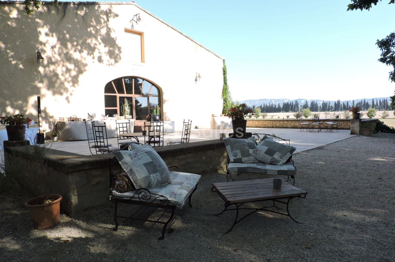 Terrasse ensoleillée avec mobilier de jardin, vue sur un paysage rural et bâtiment en pierre clair.