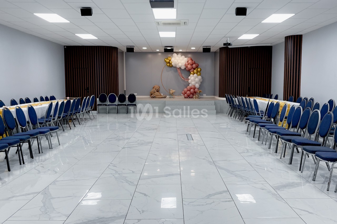 Salle de réception lumineuse avec sol en marbre, chaises bleues alignées et décoration florale sur une estrade.
