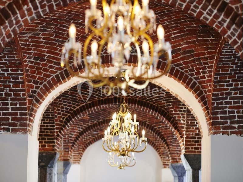 Plafond voûté en briques rouges avec des lustres dorés suspendus, éclairant un espace intérieur élégant.
