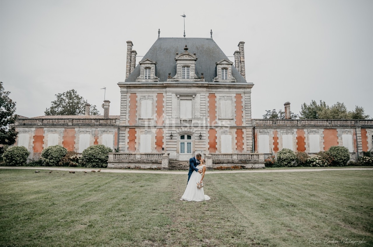 Un couple en tenue de mariage pose devant un château ancien entouré d'un grand jardin.