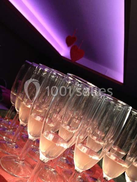 Rangée de flûtes à champagne vides alignées sur une table, éclairage violet et décorations en forme de cœurs rouges.