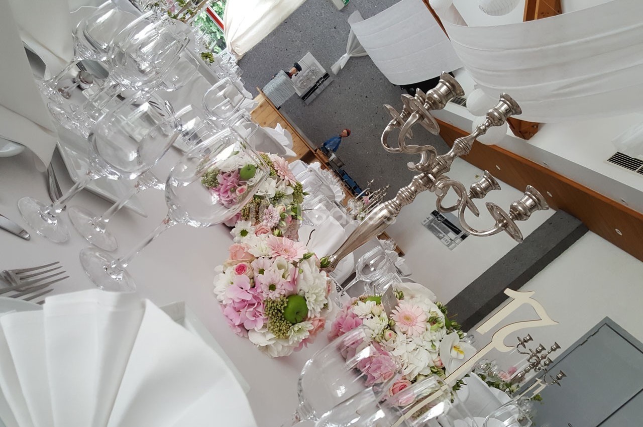 Table élégamment dressée avec des fleurs pastel, des chandeliers argentés et des verres en cristal dans une salle lumineuse.