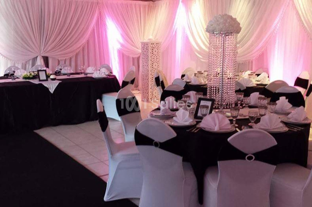 Salle de réception décorée avec des nappes noires et blanches, des chaises assorties et un éclairage rose tamisé.