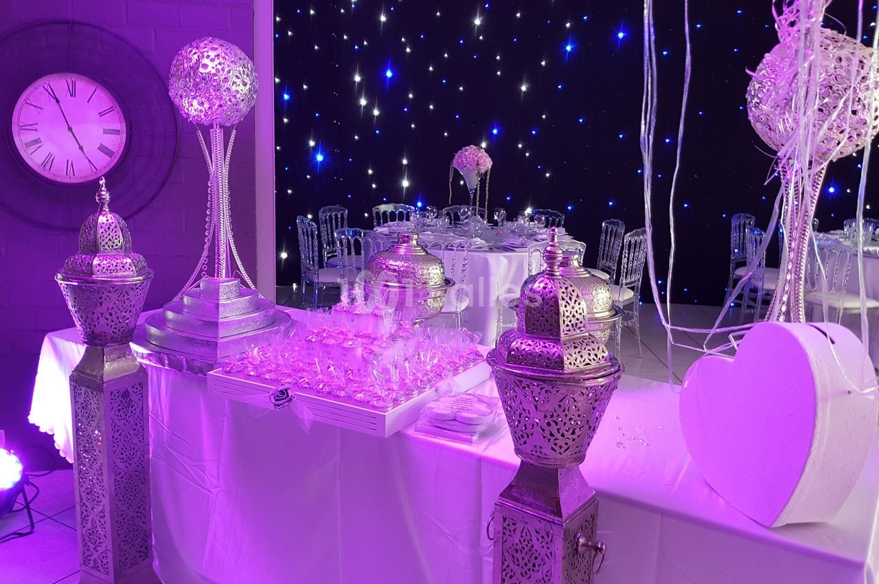 Décoration de salle avec lanternes argentées, table dressée et éclairage violet sous un fond étoilé.