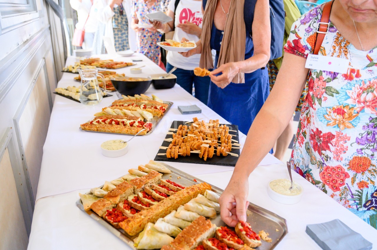 Buffet avec des plateaux de tartes salées, feuilletés et sauces, des personnes se servant en arrière-plan.