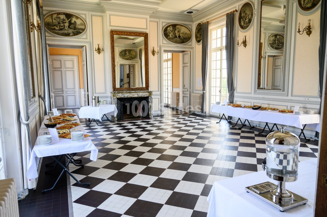 Salle élégante avec sol en damier, tables dressées pour un buffet et grandes fenêtres laissant entrer la lumière naturelle.