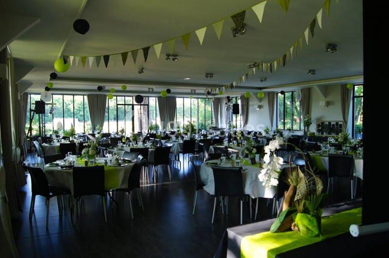 Salle de réception décorée avec des tables dressées, des guirlandes et des éléments verts et blancs.
