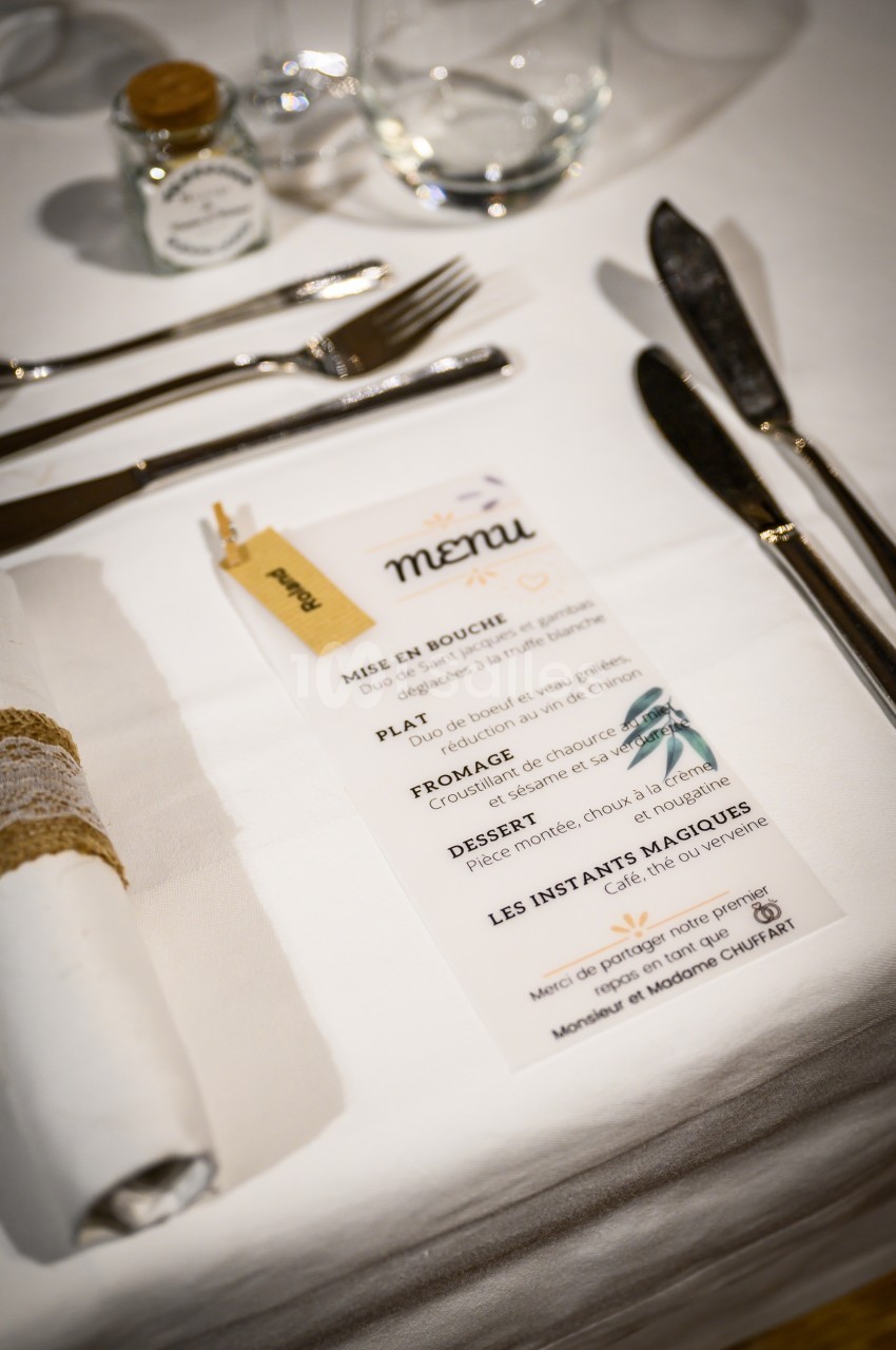 Menu imprimé posé sur une table dressée avec couverts, serviette enroulée et verre transparent.