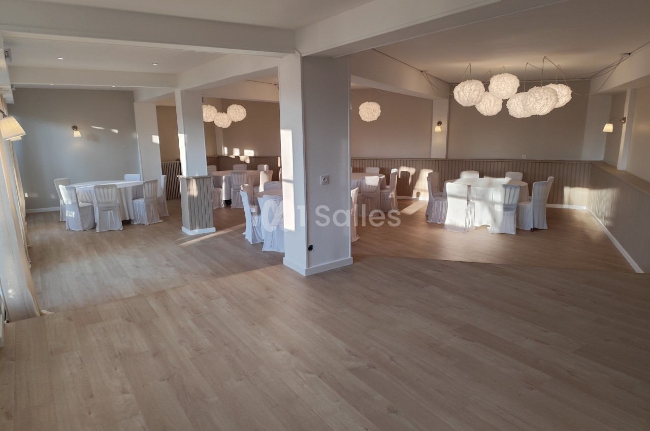 Salle lumineuse avec parquet clair, tables rondes dressées et chaises blanches, éclairée par des suspensions modernes.