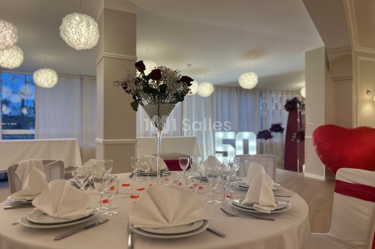 Salle décorée pour une fête, avec une table élégamment dressée, des roses et le chiffre 50 illuminé en arrière-plan.