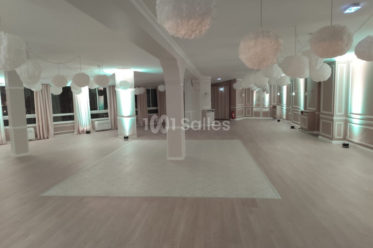Salle spacieuse avec parquet clair, colonnes blanches et suspensions décoratives en forme de nuages.