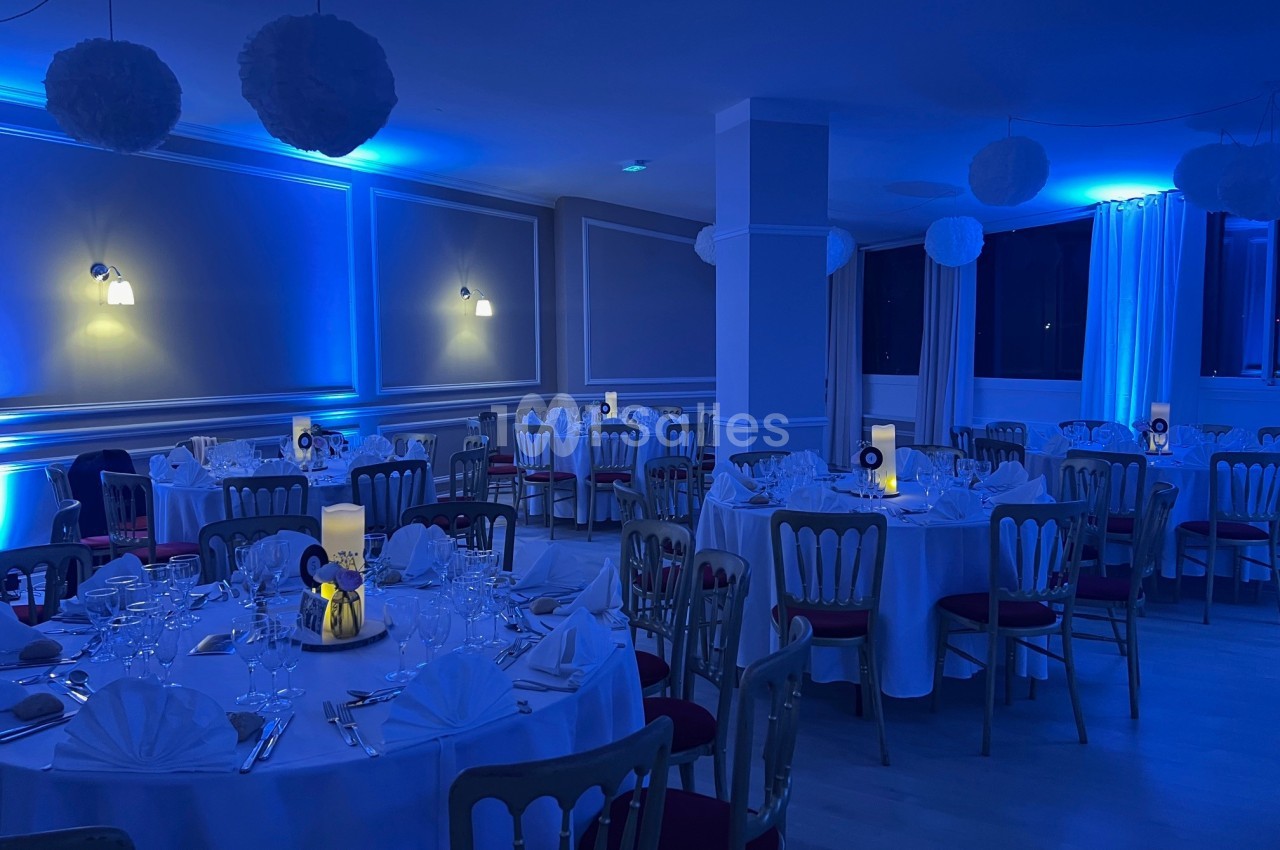 Salle de réception décorée avec des tables rondes dressées, éclairée par une lumière bleue tamisée.