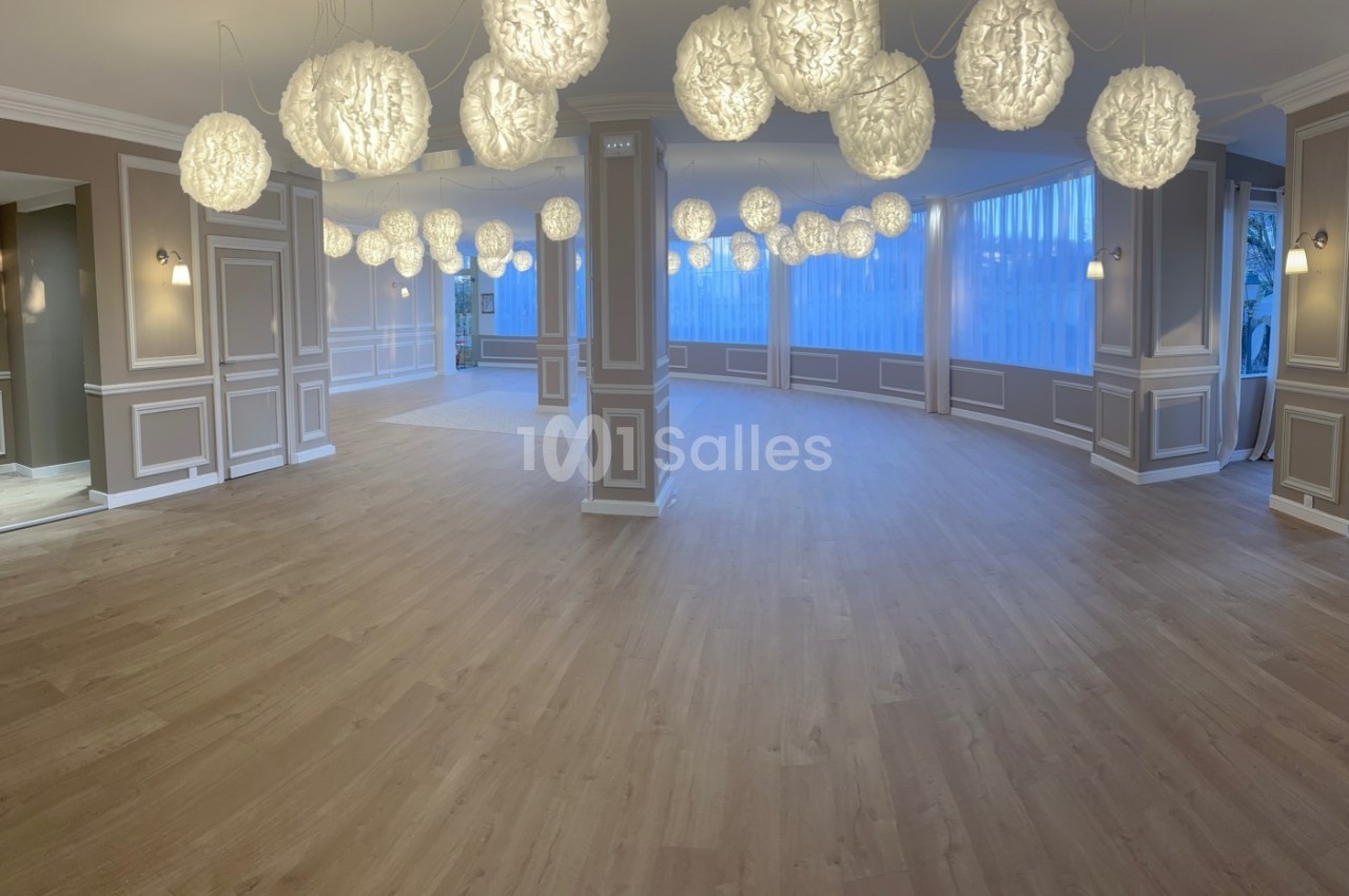 Salle spacieuse avec parquet clair, murs beige et blanc, éclairée par des suspensions lumineuses rondes.