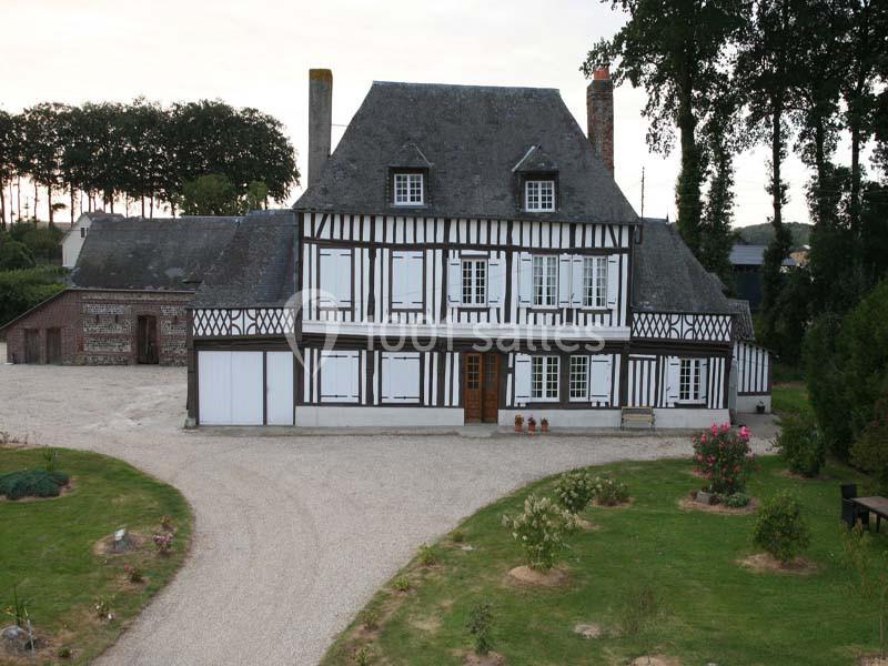 Maison à colombages traditionnelle avec toit en ardoise, entourée d'un jardin et d'une allée gravillonnée.