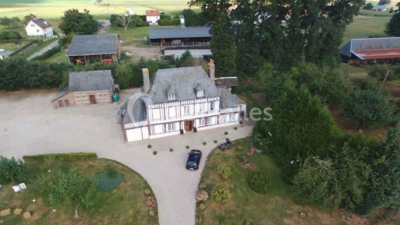 Vue aérienne d'une grande maison traditionnelle entourée de jardins, avec des bâtiments annexes et des champs à proximité.