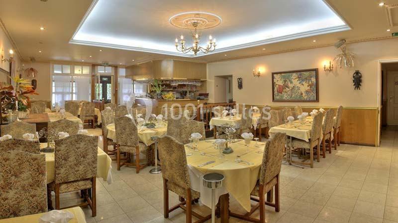 Salle de restaurant lumineuse avec tables dressées, nappes jaunes, chaises rembourrées et décoration murale.