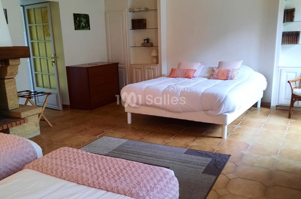 Chambre lumineuse avec un lit double, deux lits simples, une cheminée, des étagères et un sol en carrelage.