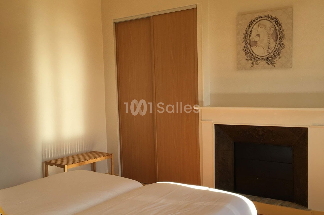 Chambre lumineuse avec deux lits simples, une cheminée décorative, un placard en bois et un tableau au mur.
