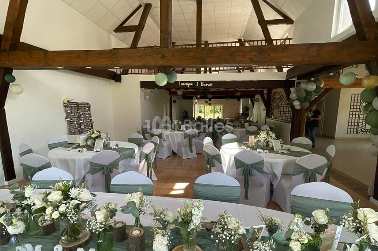 Salle de réception décorée pour un mariage, avec tables rondes ornées de nappes blanches et de centres de table floraux.
