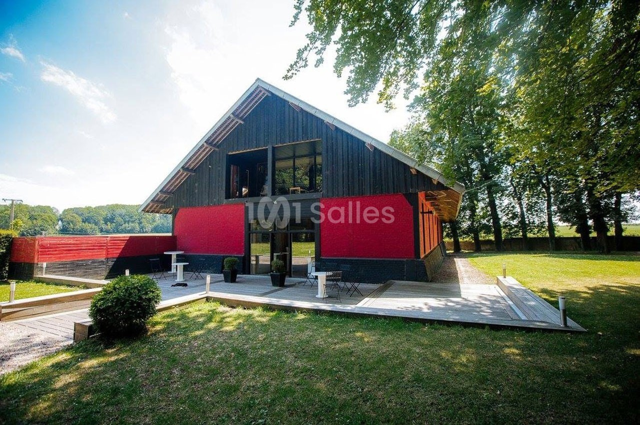 Bâtiment moderne en bois et rouge avec terrasse en bois, entouré d'arbres et d'une pelouse.