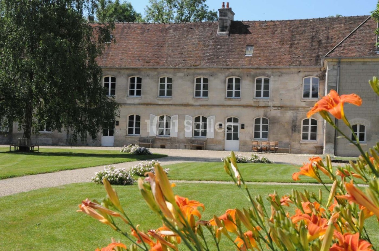 Bâtiment en pierre avec toit en tuiles, entouré de pelouse et de fleurs orange au premier plan.
