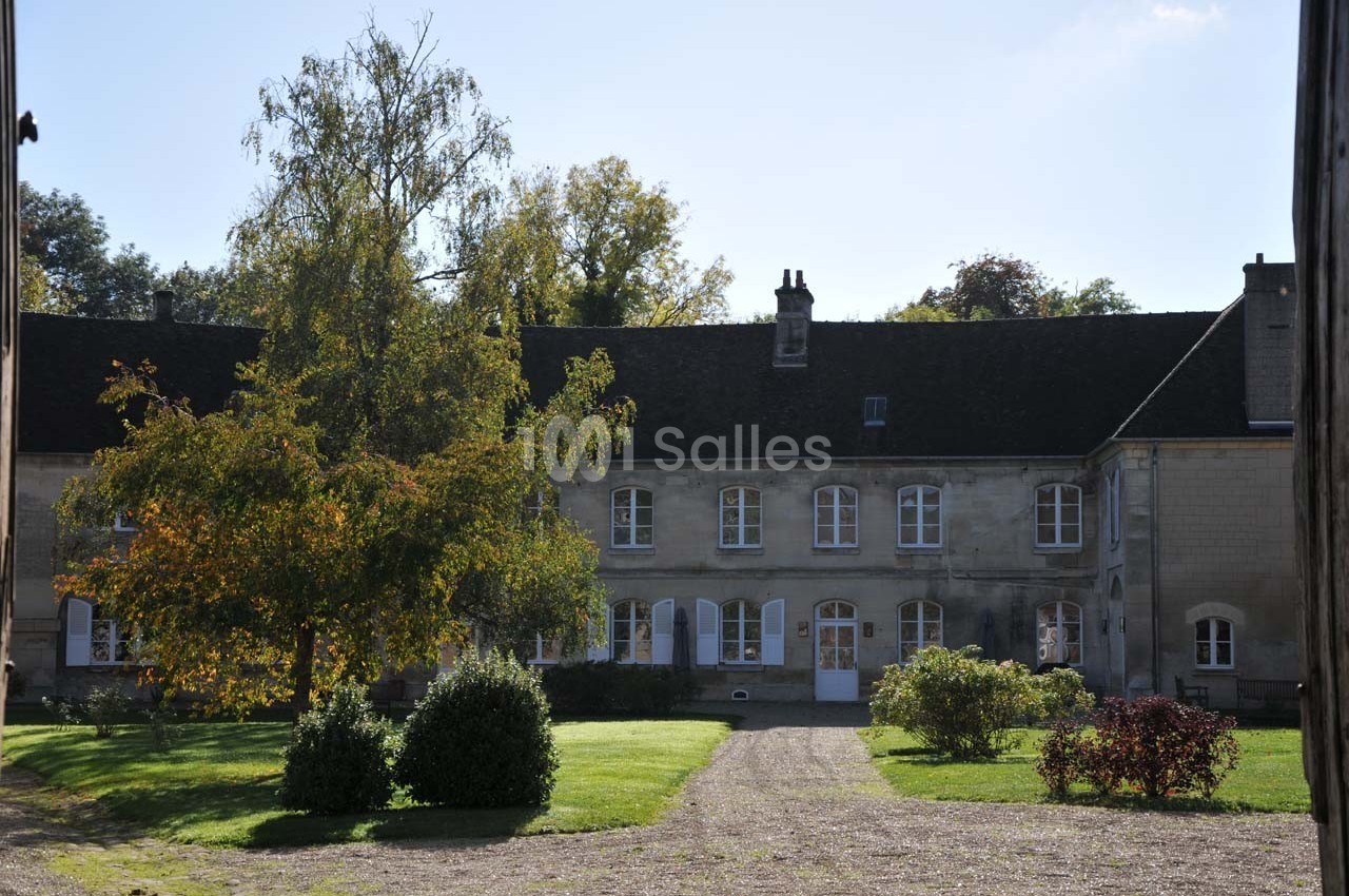 Bâtiment en pierre avec toit en ardoise, entouré d'arbres et d'un jardin, sous un ciel dégagé.