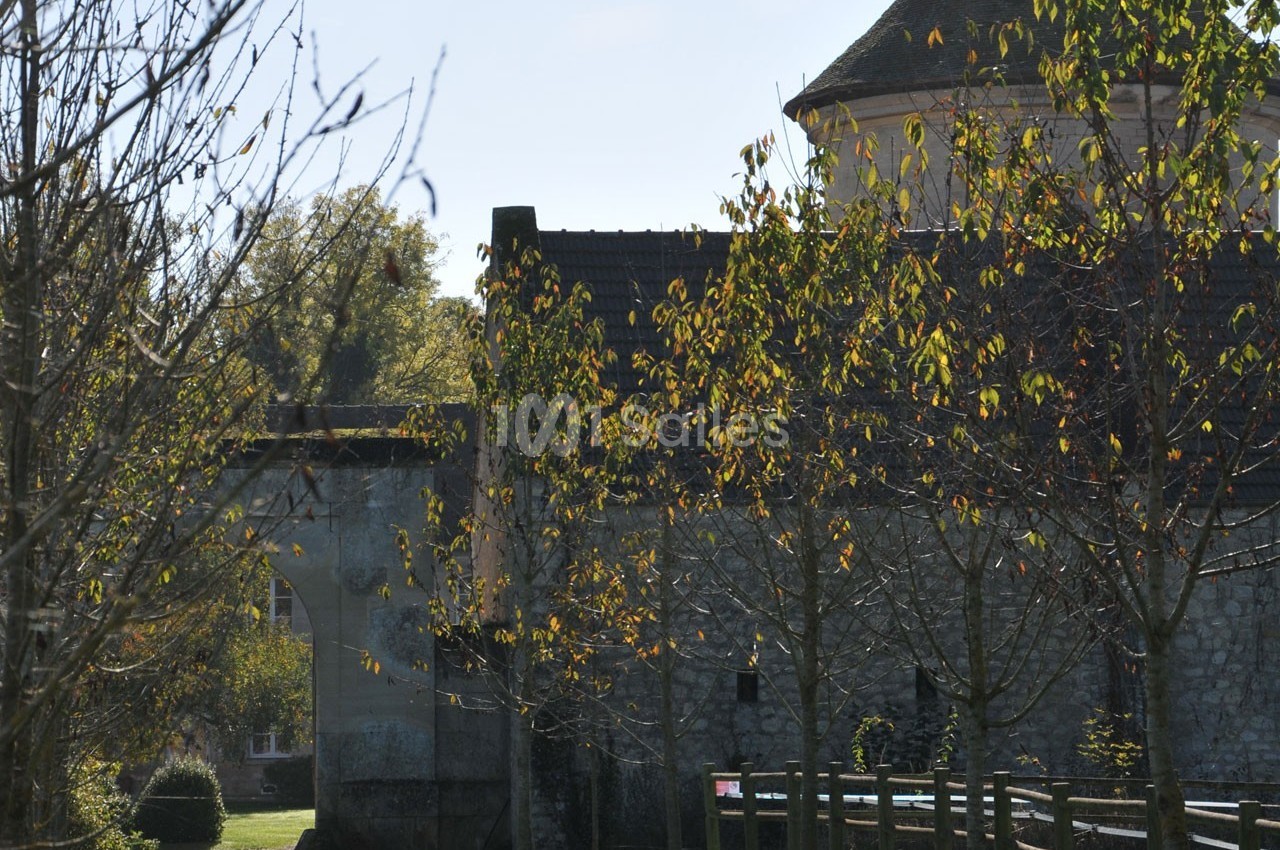 Vue d'un mur en pierre avec un porche, entouré d'arbres aux feuilles d'automne sous un ciel clair.