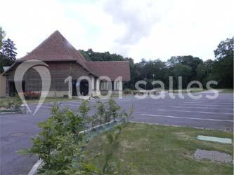 Bâtiment à toit en pente avec parking vide et espaces verts environnants, sous un ciel légèrement nuageux.