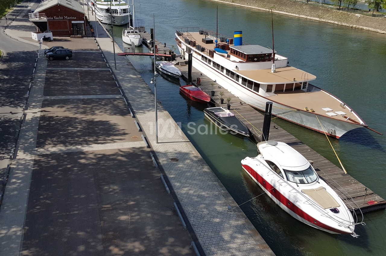Bateaux amarrés le long d'un quai sur une rivière, avec une promenade bordée d'arbres à gauche.