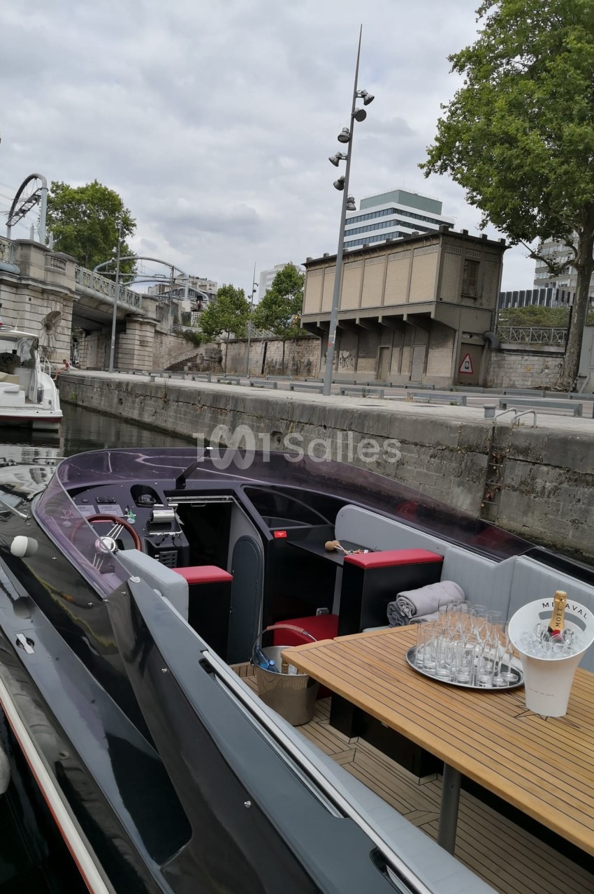 Bateau amarré le long d'un quai, avec une table dressée et des bâtiments en arrière-plan.