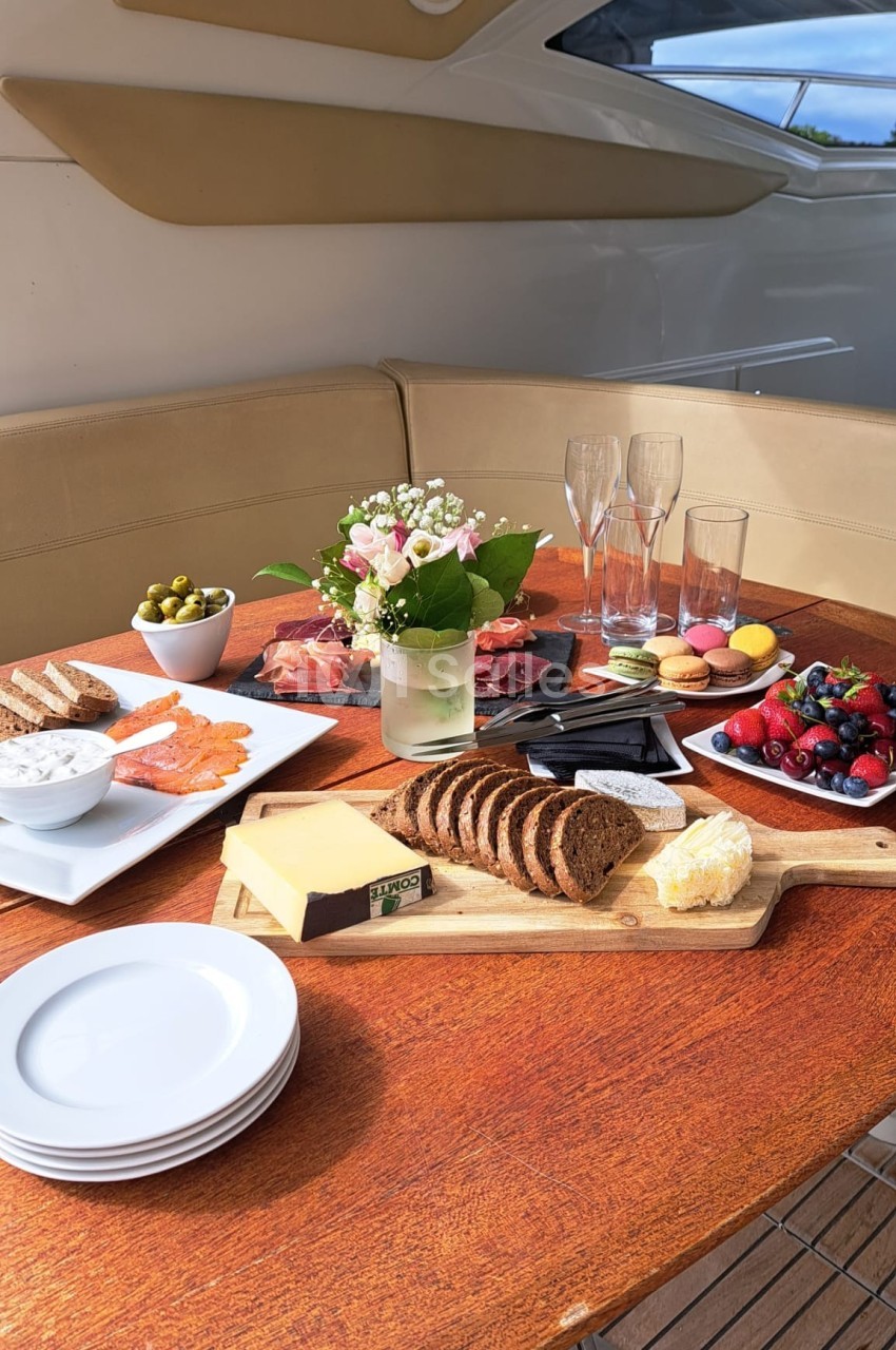 Table dressée avec des plats variés : pain, fromage, saumon fumé, fruits, olives, et verres à champagne.