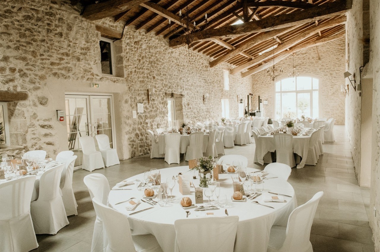 Salle de réception en pierre avec tables rondes et rectangulaires dressées pour un événement festif.