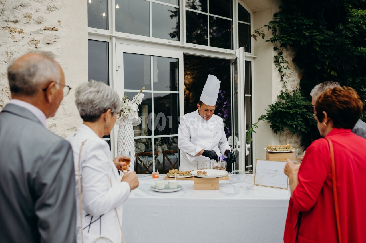 Un chef en tenue blanche prépare des plats devant un groupe de personnes lors d'un événement en extérieur.
