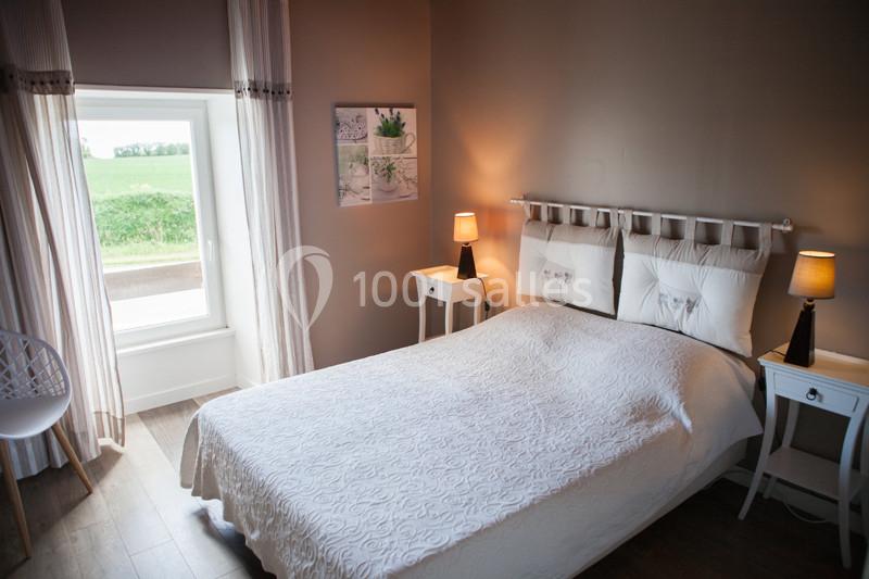 Chambre lumineuse avec un lit double, deux tables de chevet avec lampes allumées et une fenêtre donnant sur un paysage…