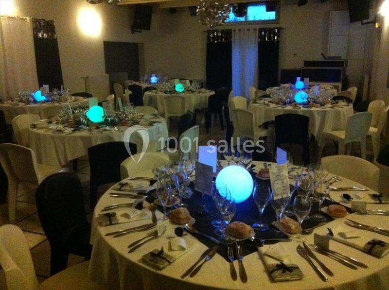 Salle de réception décorée avec des tables rondes dressées, éclairées par des centres de table lumineux colorés.