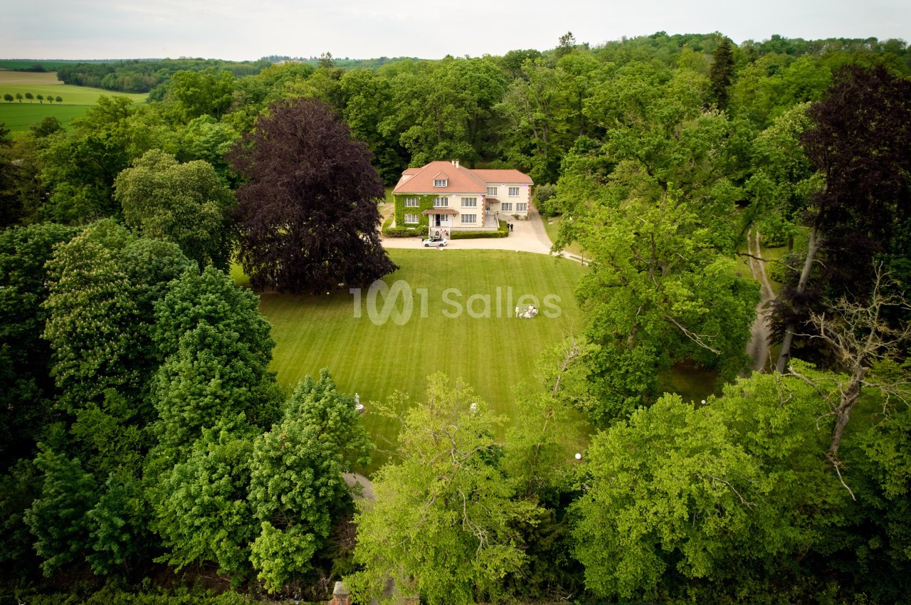 Vue aérienne d'une grande maison entourée de pelouses et d'arbres dans un cadre verdoyant.