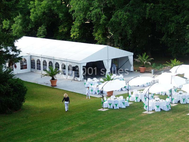 Grande tente blanche avec tables et chaises décorées sous des parasols, installées sur une pelouse près d'arbres.