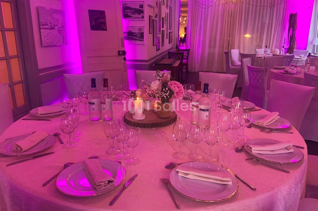 Table élégamment dressée pour un dîner, avec nappes roses, verres, couverts, bougie et décoration florale.