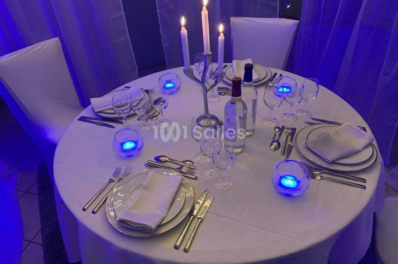 Table ronde élégamment dressée avec nappes blanches, chandeliers allumés et vaisselle raffinée dans une ambiance lumineuse…