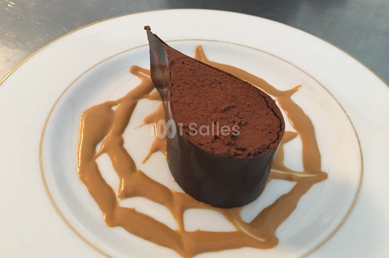 Dessert au chocolat en forme de goutte, entouré d'un décor de sauce caramel sur une assiette blanche.