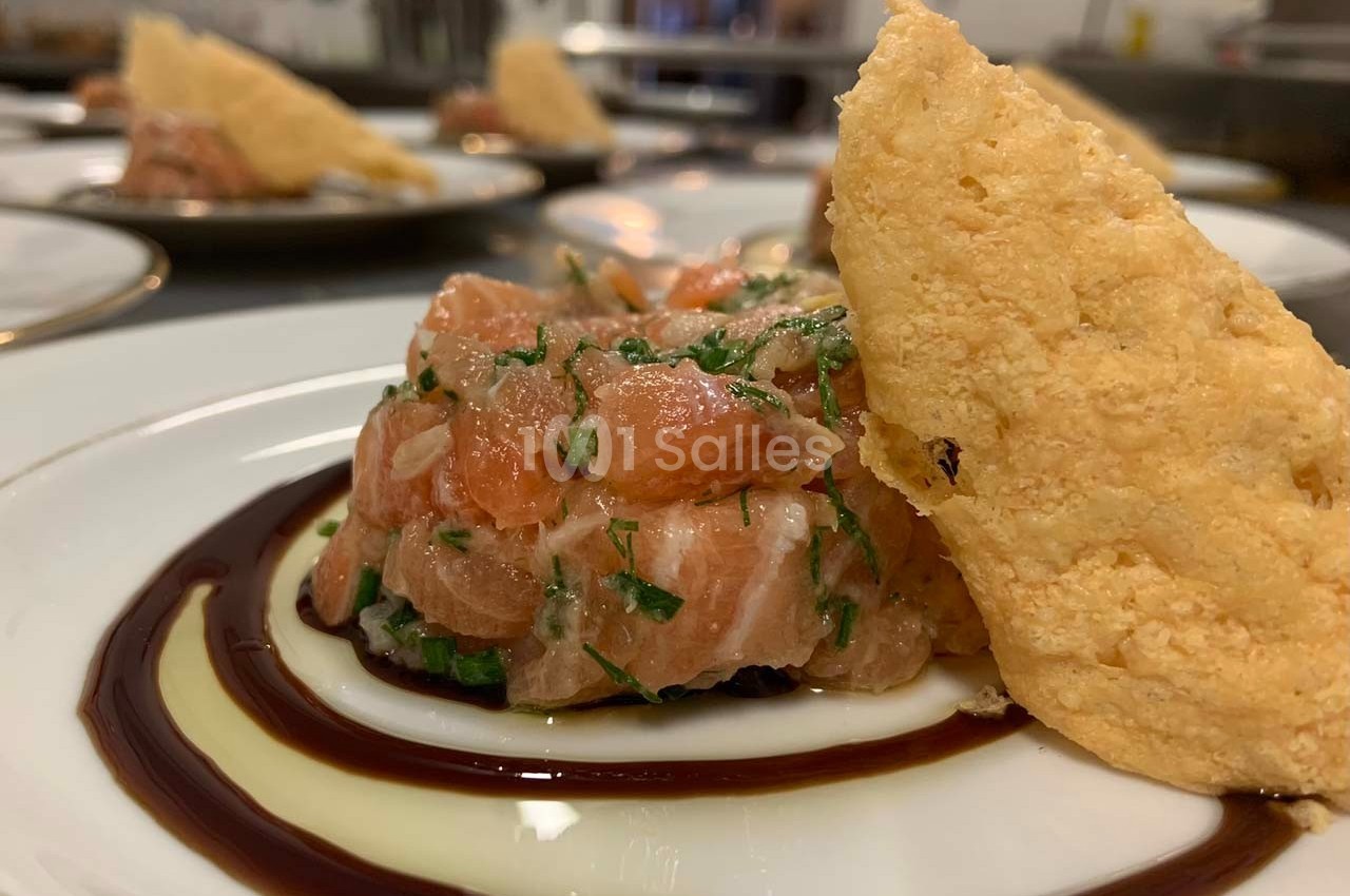 Tartare de saumon frais avec herbes, dressé sur une assiette avec un filet de sauce et une tuile croustillante.