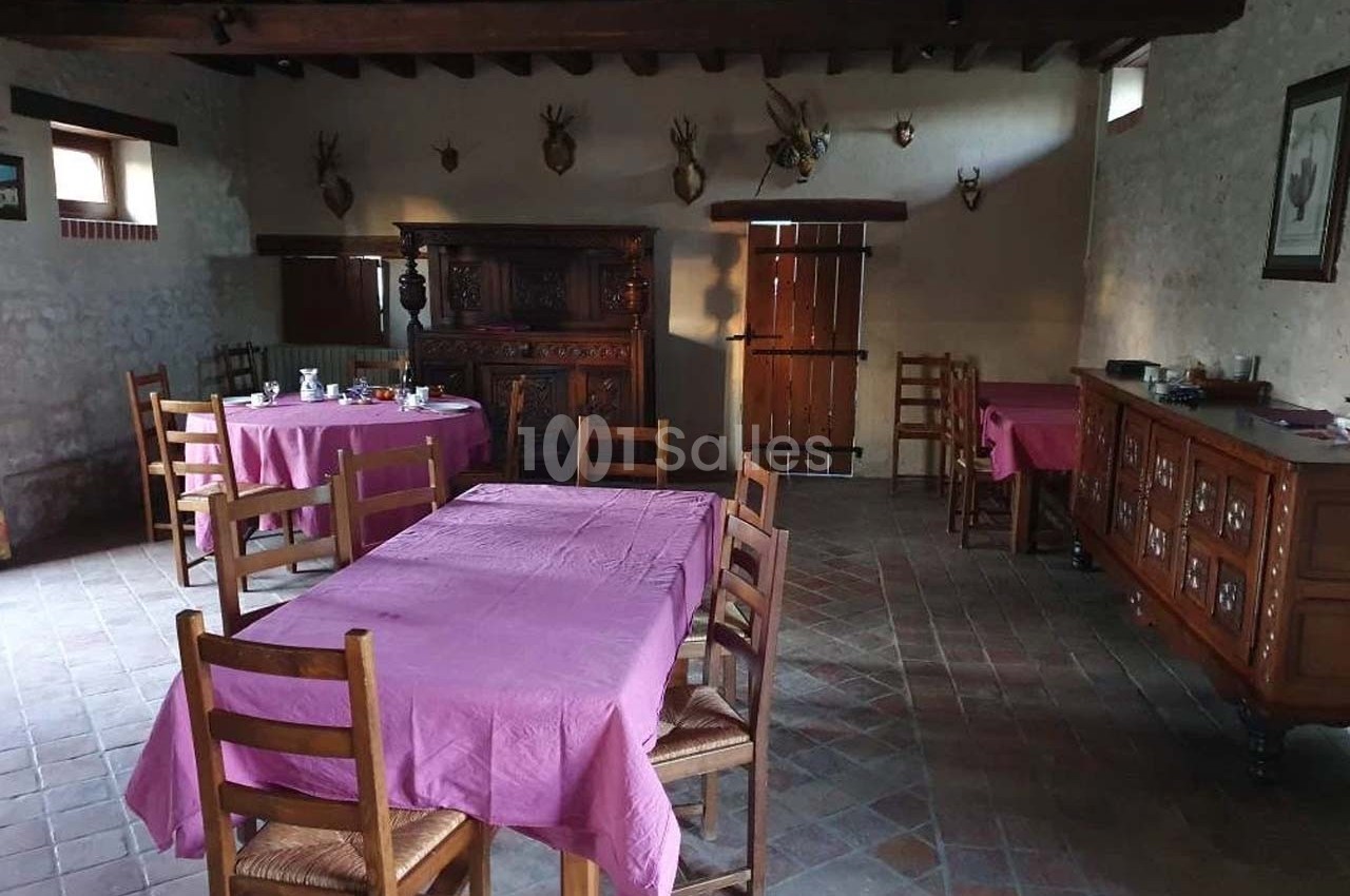 Salle à manger rustique avec tables recouvertes de nappes violettes, meubles en bois et décoration murale avec trophées.