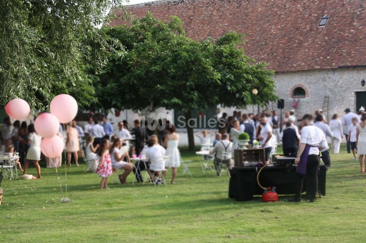 Groupe de personnes rassemblées dans un jardin pour un événement, avec des ballons roses et des tables installées.