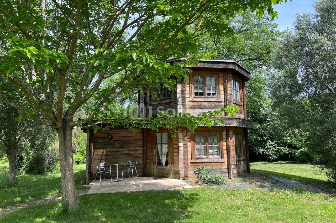 Maison en bois à deux étages entourée d'arbres, avec une terrasse équipée de chaises et d'une table.