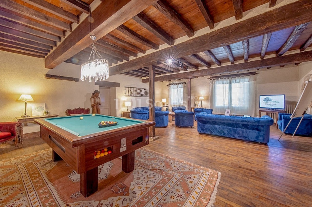 Salle de séjour spacieuse avec billard, canapés bleus, poutres apparentes et lumière naturelle.