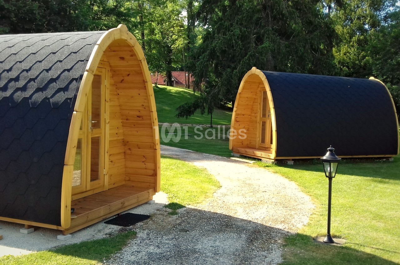 Deux cabanes en bois en forme d'arche avec toits noirs, situées sur une pelouse entourée d'arbres.